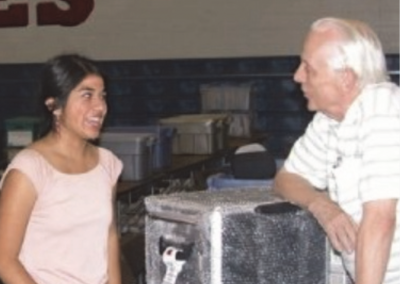 Ron Underwood talking with a student during a speech and debate tournament, reflecting his lifelong dedication to supporting and encouraging young competitors.
